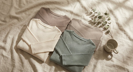 A flat lay of ribbed long sleeve tops in neutral tones arranged on a linen surface in soft natural light.